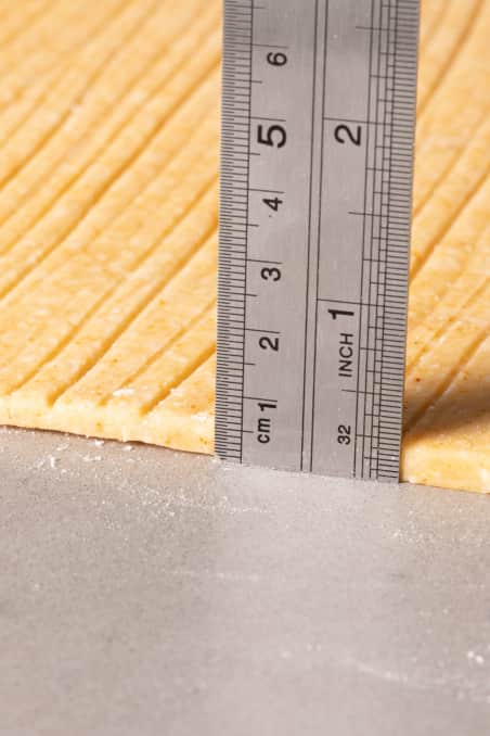Closeup of stainless-steel ruler measuring thickness of Southern Cheese Straw dough.